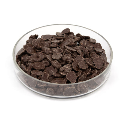 Dark chocolate melts piled in a clear glass bowl on a white background.