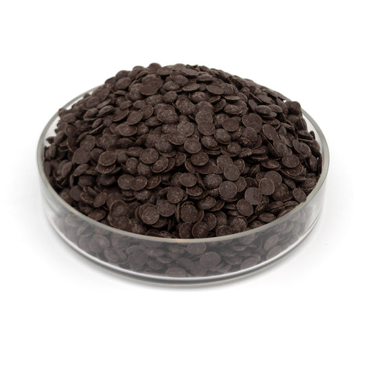 Dark chocolate drops piled in a clear glass bowl on a white background.