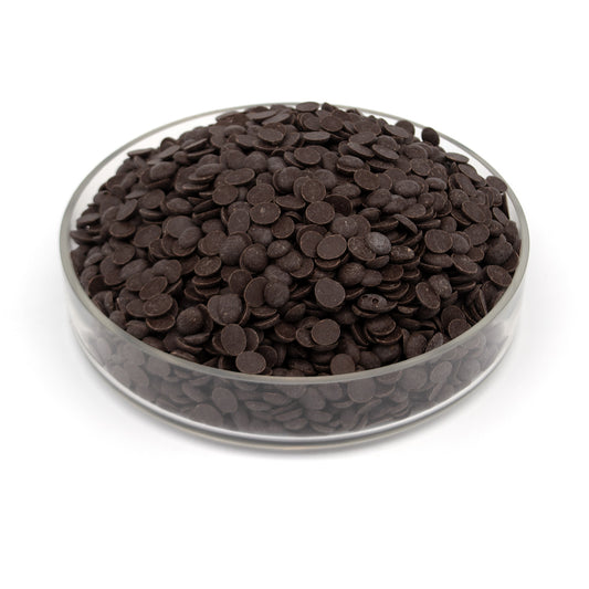 Dark chocolate discs piled in a clear glass bowl on a white background.