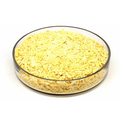 Cacao butter shavings piled in a clear round glass bowl on a white background.