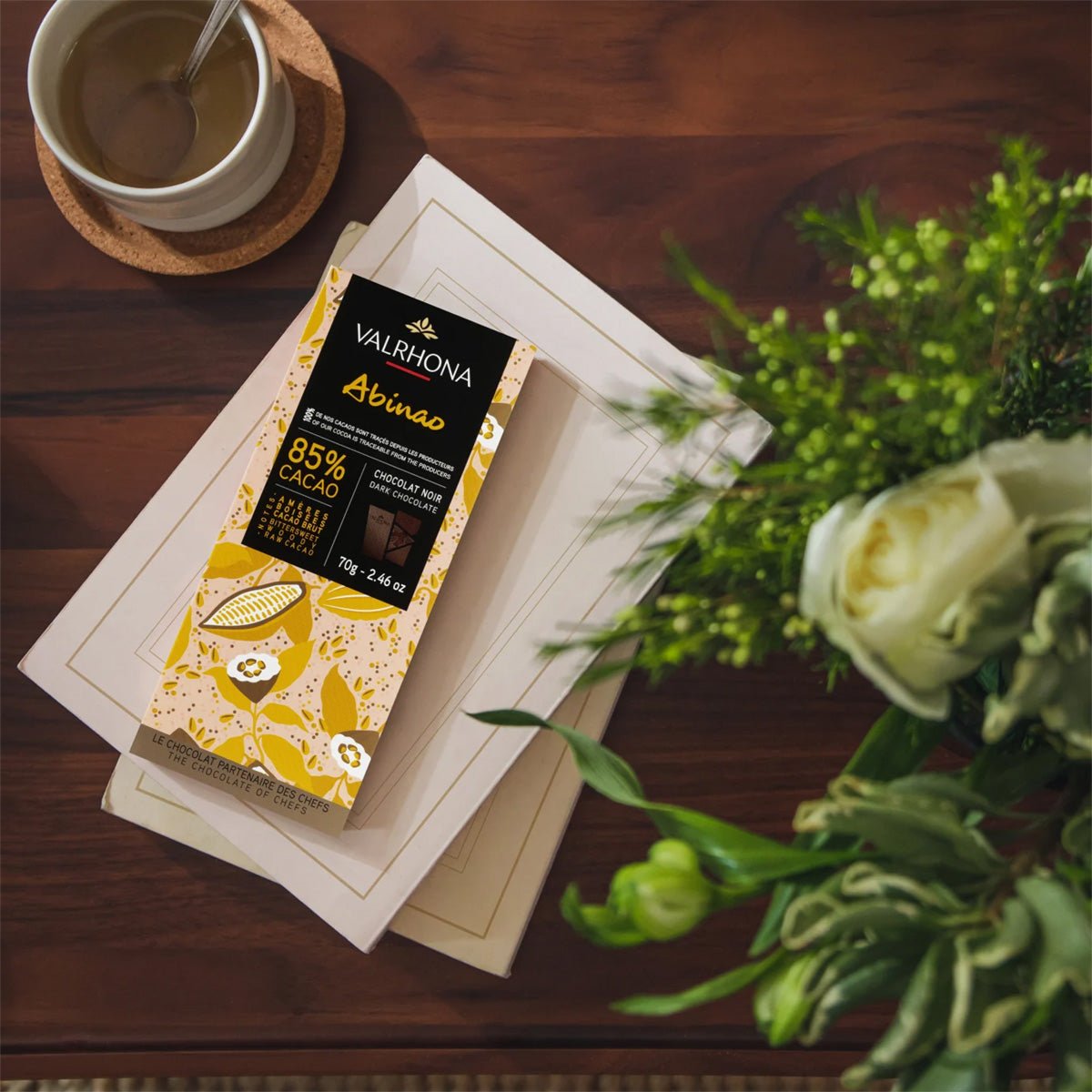 Valrhona chocolate bar on a wooden table with a cup of coffee and flowers.