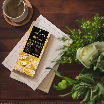 Valrhona chocolate bar on a wooden table with a cup of coffee and flowers.