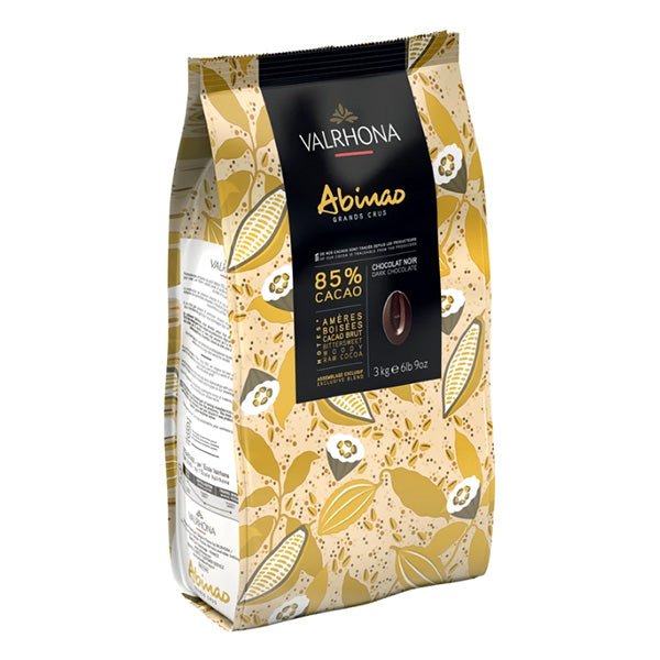 A package of Valrhona Abinao Les Feves 85% Dark Chocolate Couverture Discs with a decorative pattern of chocolate pieces and leaves in gold and brown colors.