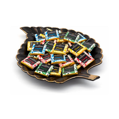 Assorted Valrhona chocolate squares on a decorative black plate with a white background