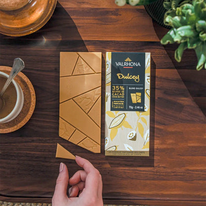 Valrhona Dulcey chocolate bar packaging on a wooden table with a hand reaching towards it.