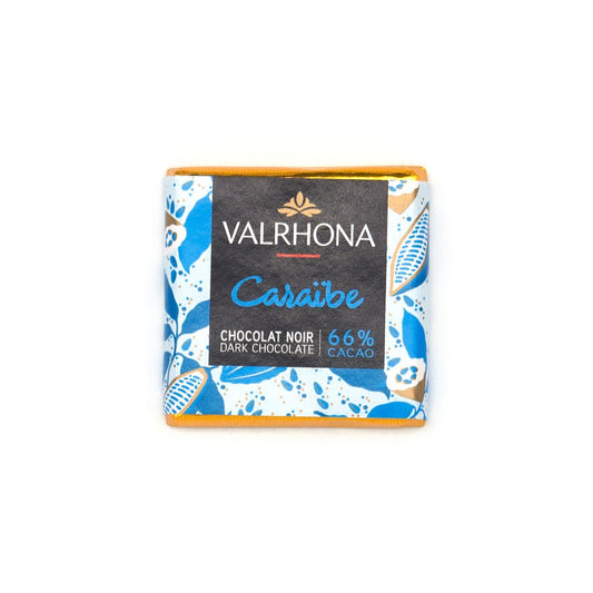 A Valrhona Caraibe dark chocolate napolitain in its wrapper, featuring a black center label with blue and gold accents and a blue-and-white patterned border, set against a plain white background.