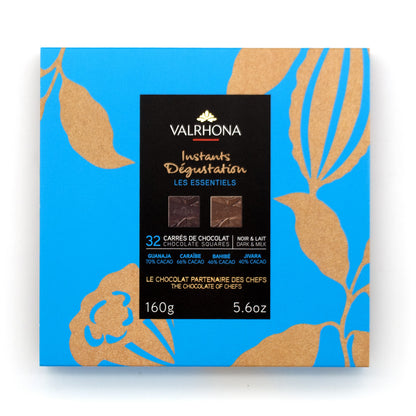 A square box of Valrhona Instantis Dégustation Les Essentiels chocolate squares, featuring a bright blue background with gold botanical leaf patterns and a central black label.
