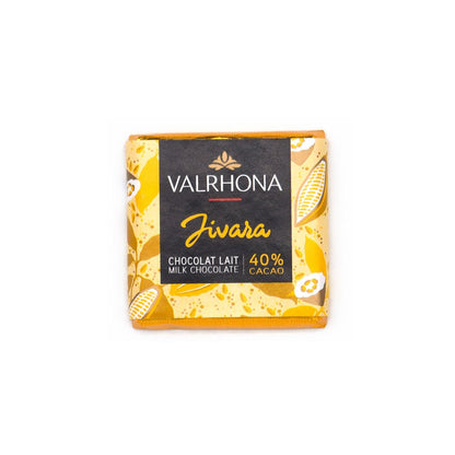 A square Valrhona Jivara milk chocolate napolitain with 40% cacao, wrapped in a yellow and gold patterned paper sleeve with a black central label.