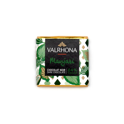 A Valrhona Manjari chocolate napolitain wrapped in a decorative green and white patterned paper sleeve with gold foil edges, centered on a plain white background.