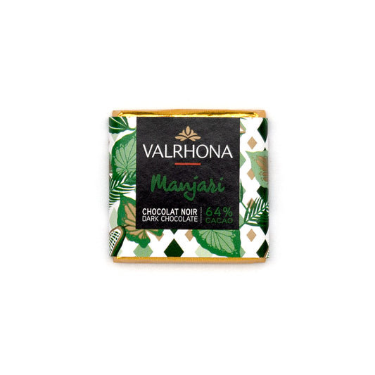 A Valrhona Manjari chocolate napolitain wrapped in a decorative green and white patterned paper sleeve with gold foil edges, centered on a plain white background.