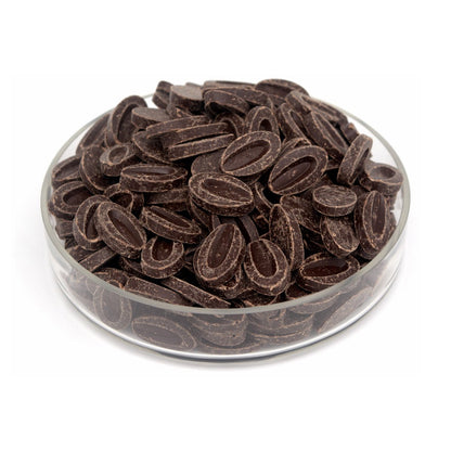 Dark chocolate disc-shaped chocolates piled in a clear glass bowl on a white background.