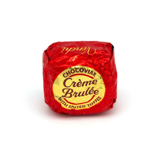 A single wrapped chocolate cookie on a white background, wrapped in red foil with a gold and red label that reads 'CHOCOVIAR Crème Brûlée WITH SALTED TOFFEE'.